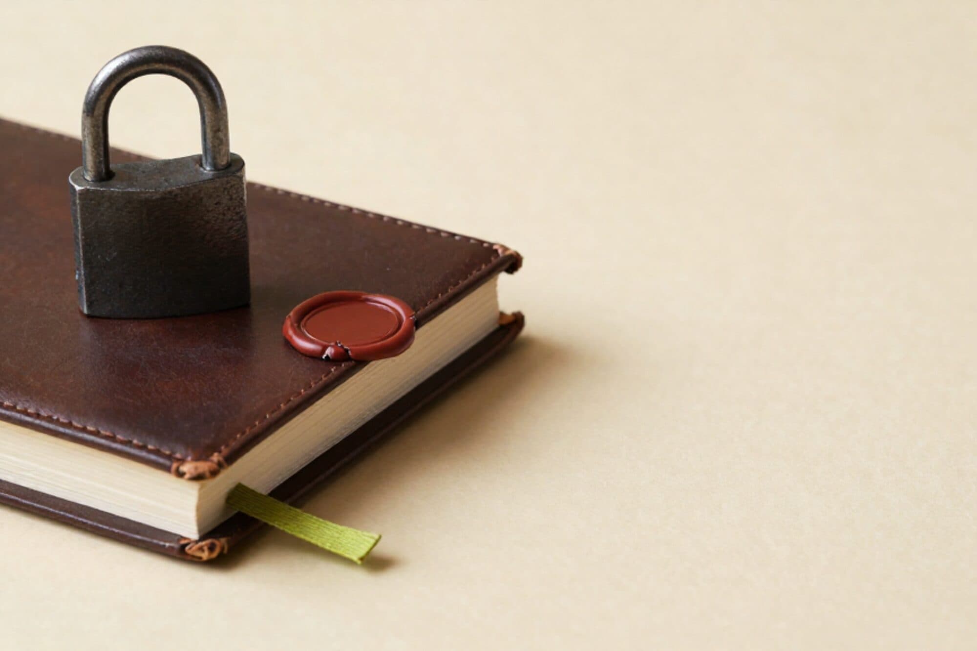 IJzeren hangslot dicht op een gesloten leren logboek op ivoorkleurig papier, een dun groen lint en gebarsten rood waszegel ernaast