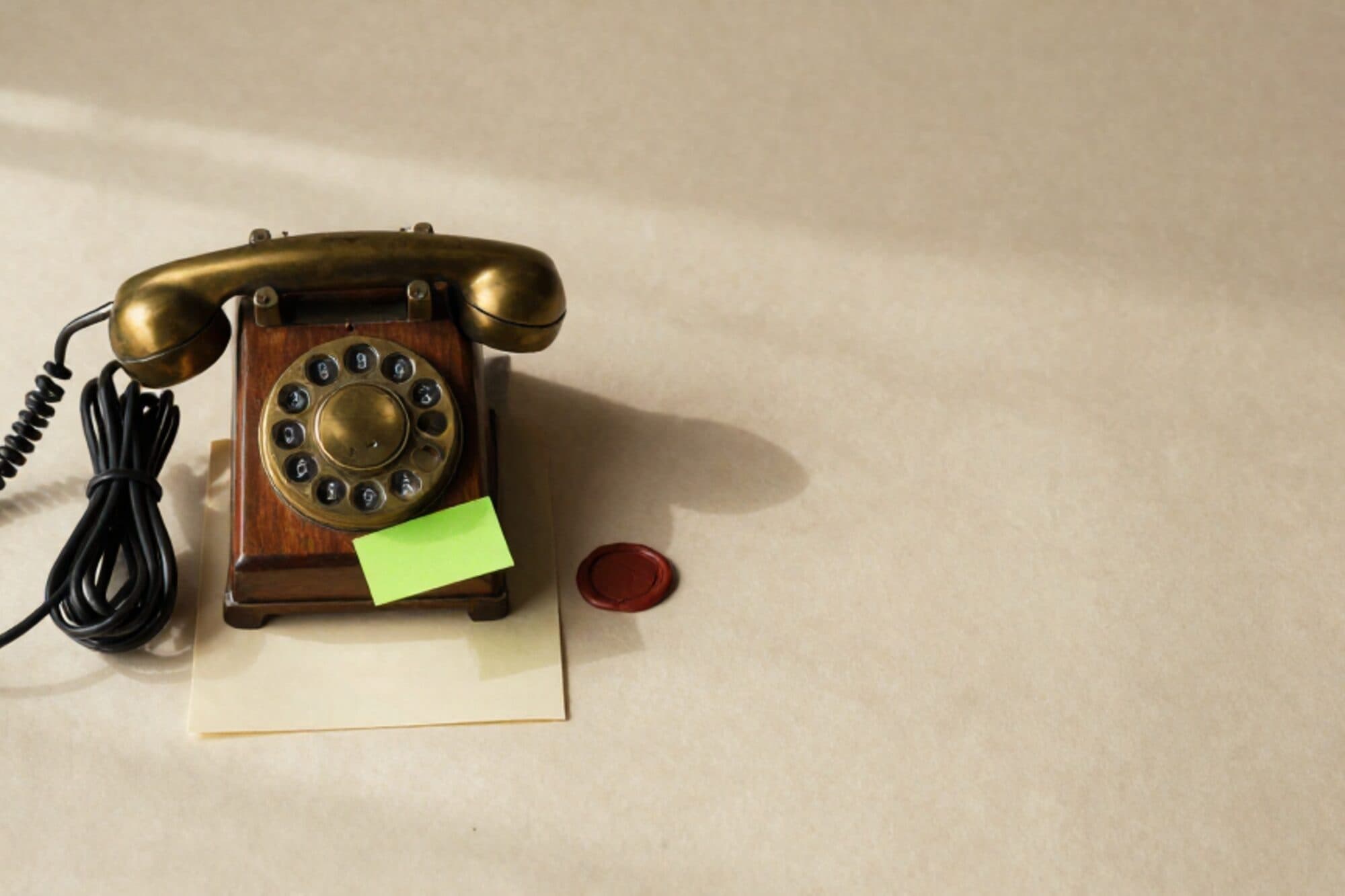 Vintage telefoonschakelbord van messing en hout op ivoorkleurig papier, zes opgerolde patchkabels, papieren formulier met groene memo, rode lakzegel.