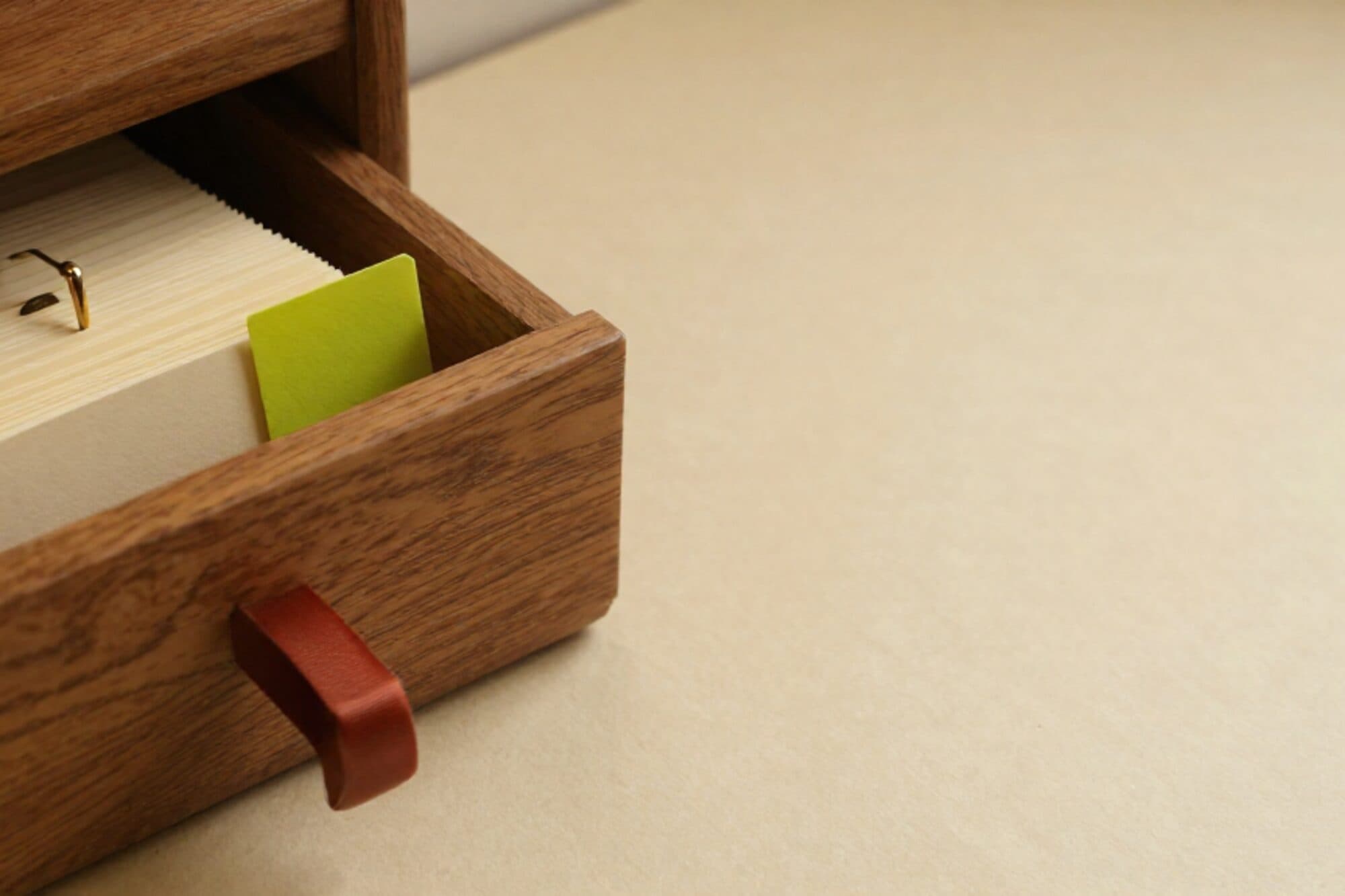 Open eikenhouten kaartenlade met crème kaarten, koperen scheider, groene tabkaart en rood lint op ivoor papier.