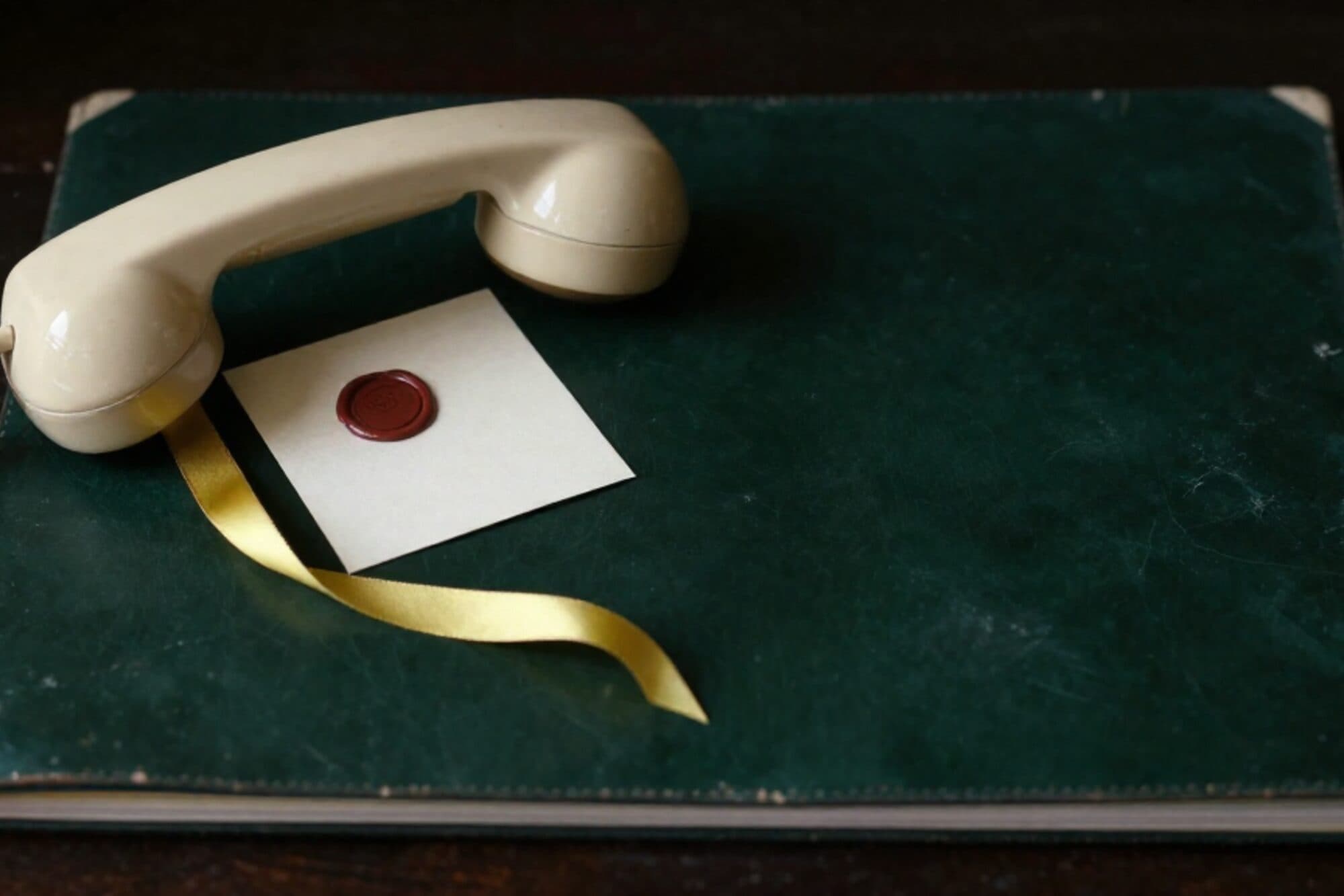 Crème bakelieten telefoonhoorn op groen leren onderlegger, limoengroen lint, ivoren kaart met rood wax zegel.